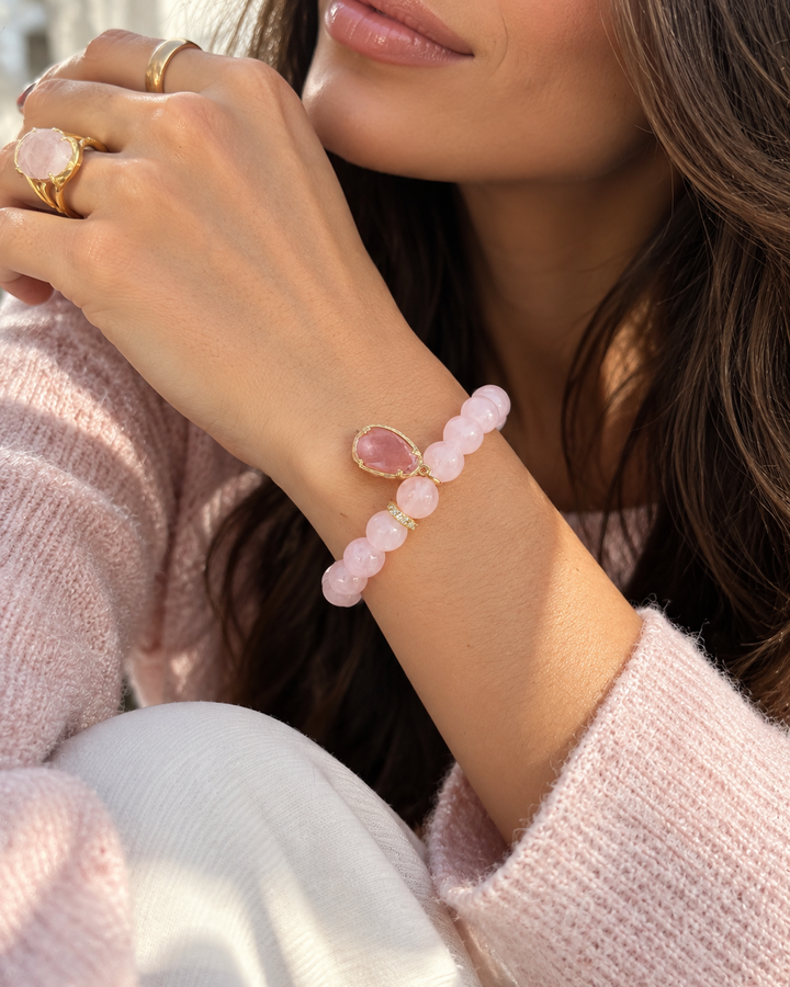 Sievišķīga dabīgā rozā kvarca rokassprādze ar maigi rozā pērlītēm un zeltītām detaļām, kas papildina romantisku un elegantu ikdienas tēlu.
