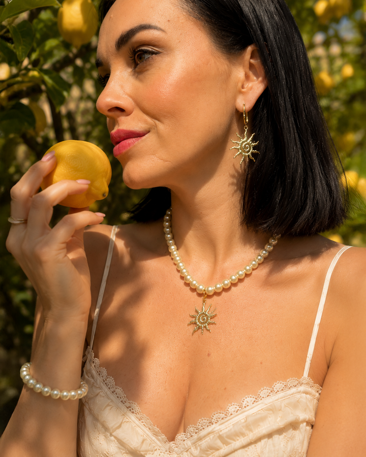Eleganta pērļu kaklarota ar saules kulonu un akcentējoši saules formas auskari luxury jewelry aesthetic stilā. Rotas veidotas siltā zelta tonī un papildinātas ar pērļu pērlītēm, radot izsmalcinātu un sievišķīgu tēlu. Ideāli piemērotas vakara outfitiem, fashion editorial fotosesijām un romantiskam soft glam stilam.
