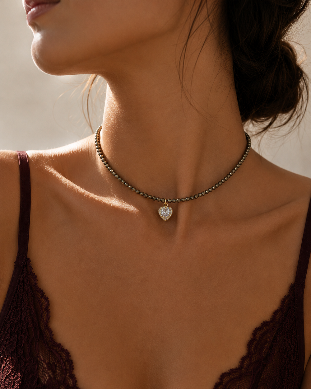 Sievietes kakla un dekoltē tuvplāns ar smalku 3 mm pirīta choker kaklarotu un mirdzošu sirds formas piekariņu
