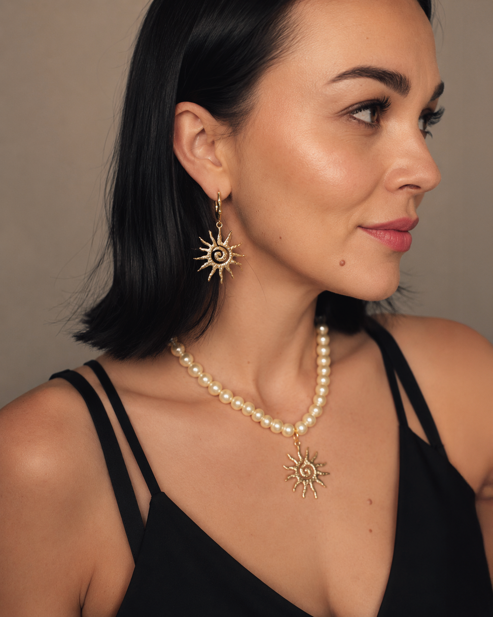 Eleganta pērļu kaklarota ar saules kulonu un akcentējoši saules formas auskari luxury jewelry aesthetic stilā. Rotas veidotas siltā zelta tonī un papildinātas ar pērļu pērlītēm, radot izsmalcinātu un sievišķīgu tēlu. Ideāli piemērotas vakara outfitiem, fashion editorial fotosesijām un romantiskam soft glam stilam.
