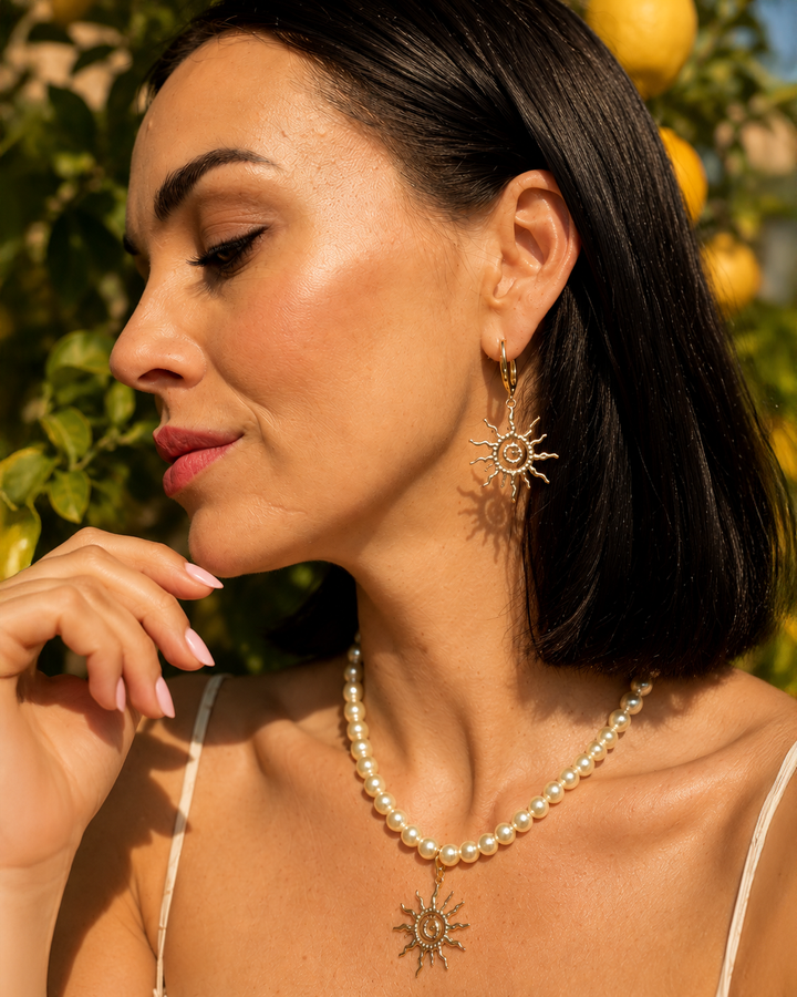 Eleganta pērļu kaklarota ar saules kulonu un akcentējoši saules formas auskari luxury jewelry aesthetic stilā. Rotas veidotas siltā zelta tonī un papildinātas ar pērļu pērlītēm, radot izsmalcinātu un sievišķīgu tēlu. Ideāli piemērotas vakara outfitiem, fashion editorial fotosesijām un romantiskam soft glam stilam.