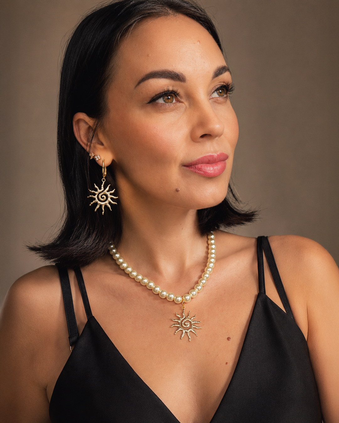 Eleganta pērļu kaklarota ar saules kulonu un akcentējoši saules formas auskari luxury jewelry aesthetic stilā. Rotas veidotas siltā zelta tonī un papildinātas ar pērļu pērlītēm, radot izsmalcinātu un sievišķīgu tēlu. Ideāli piemērotas vakara outfitiem, fashion editorial fotosesijām un romantiskam soft glam stilam.