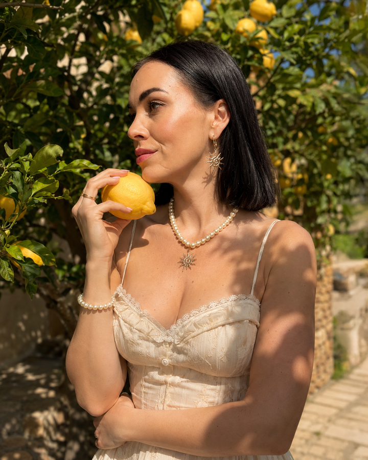 Eleganta pērļu kaklarota ar saules kulonu un akcentējoši saules formas auskari luxury jewelry aesthetic stilā. Rotas veidotas siltā zelta tonī un papildinātas ar pērļu pērlītēm, radot izsmalcinātu un sievišķīgu tēlu. Ideāli piemērotas vakara outfitiem, fashion editorial fotosesijām un romantiskam soft glam stilam.