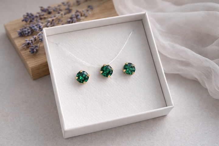 Alt teksts:

Minimālistiska rotu komplekta produktu fotogrāfija baltā kastītē – zeltītā ietvarā iestrādāti smaragdzaļi kristāli. Komplektā nagliņu auskari un kaklarota uz caurspīdīgas auklas. Fons gaišs ar koka dēlīti, žāvētu lavandu un viegli plīvojošu caurspīdīgu audumu, maigs dabīgais apgaismojums un sekls asuma dziļums.
