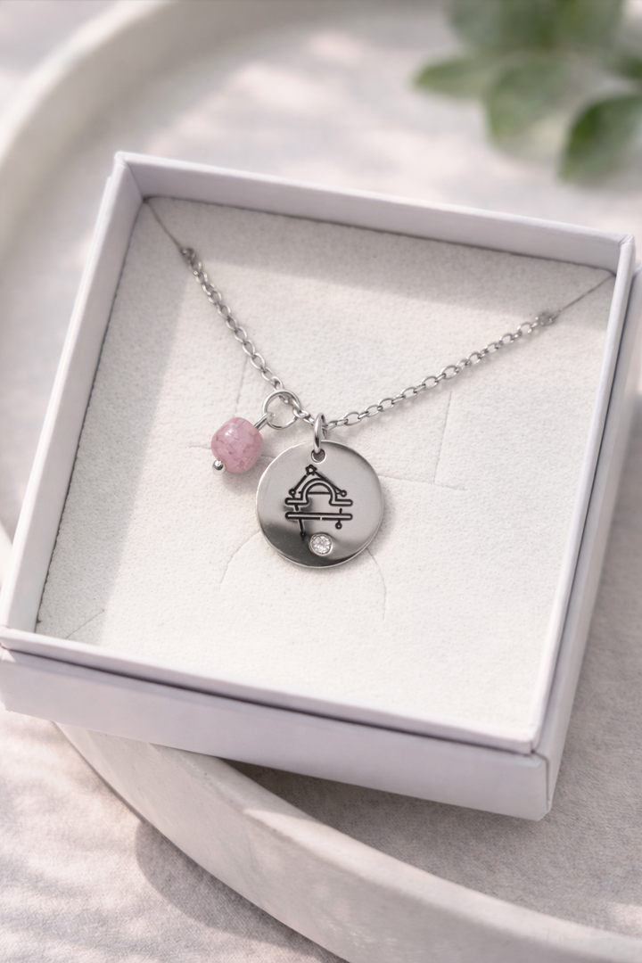 sudraba krāsas kaklarota ar apaļu medljonu un svaru zīmes gravējumu un pie kaklarotas piestiprināts dabīgais rozā turmalīns.